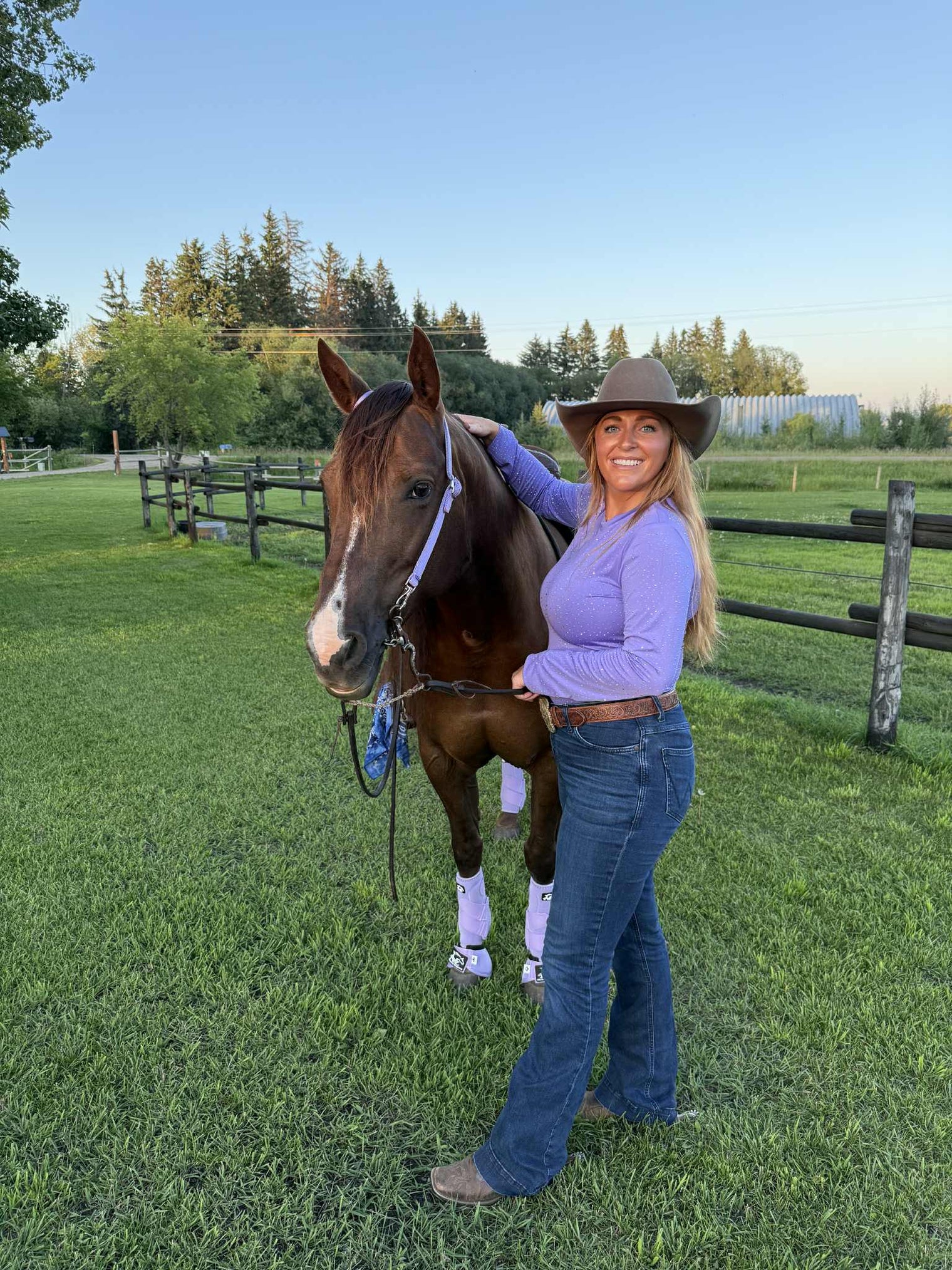 Woman in a cowboy hat waring a lavenfer bodysuit that matches her horse's lavender Alliance Equine V20x boots and bell boots.