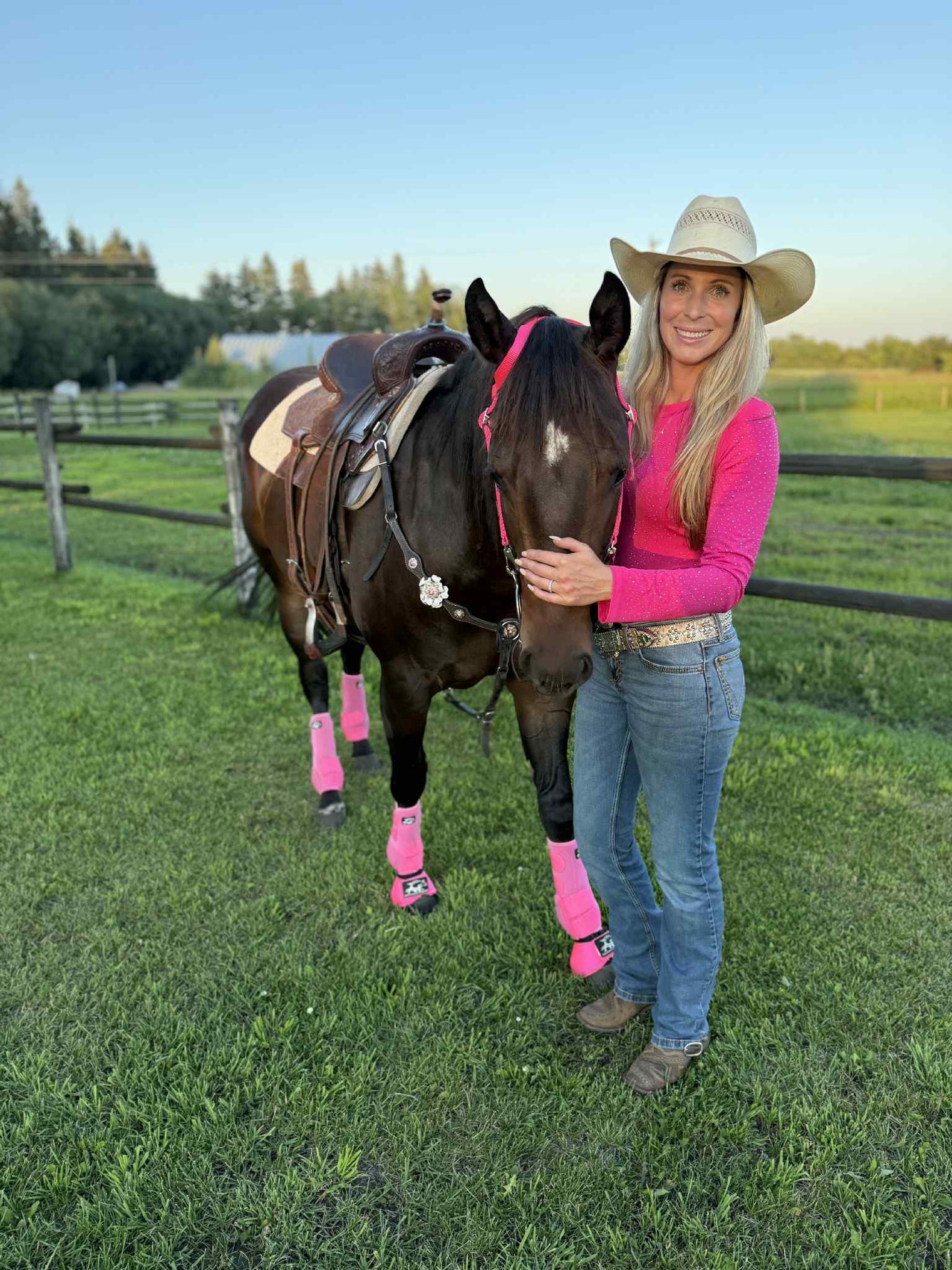Woman in a cowboy hat wearing a pink bodysuit that matches her horse's pink Alliance Equine V20x hhorse boots and bell boots.