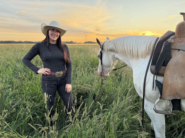 Woman in a cowboy hat wearing a black bodysuit that matches her horse's black Alliance Equine V20x hhorse boots and bell boots.