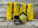 Four yellow horse leg boots and one matching horse boot wrap arranged on a rustic gray wooden plank surface. The boots feature black and white branding patches for 'Alliance Equine'.