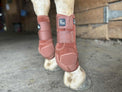 Horse legs wearing brown protective boots with 'V20x' branding in a stable setting.